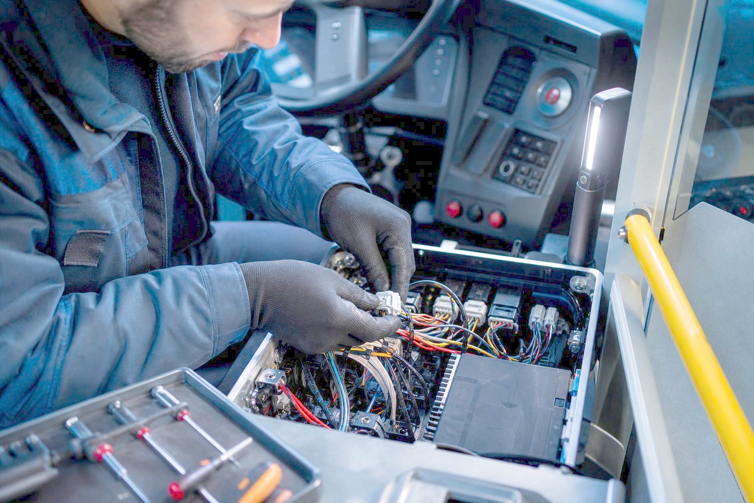 Technicien raccordant un faisceau de câbles à un calculateur embarqué dans le poste de conduite d'un bus urbain